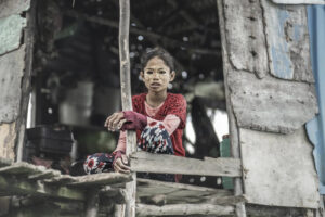 Malaysia, Denawan island, 2024-05-09. Young Bajau girl with her protective mask in front of her stilt house in a Bajau v