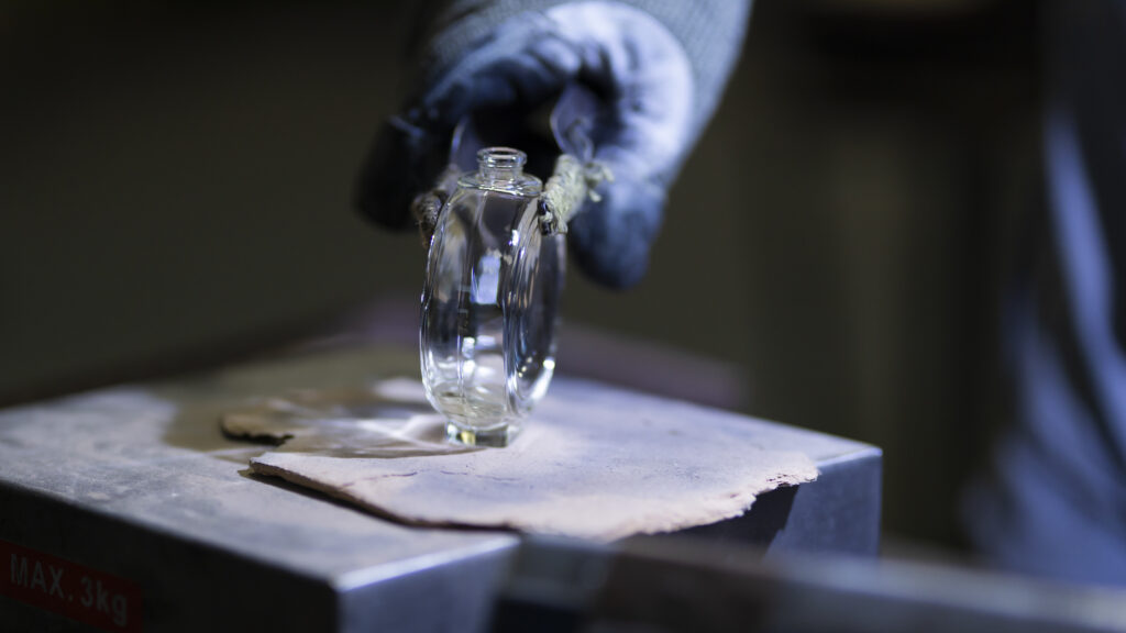France, Blangy-sur-Bresle, 2022-03-24. A blue gloved hand holds a small glass bottle on a workbench against a dark backg
