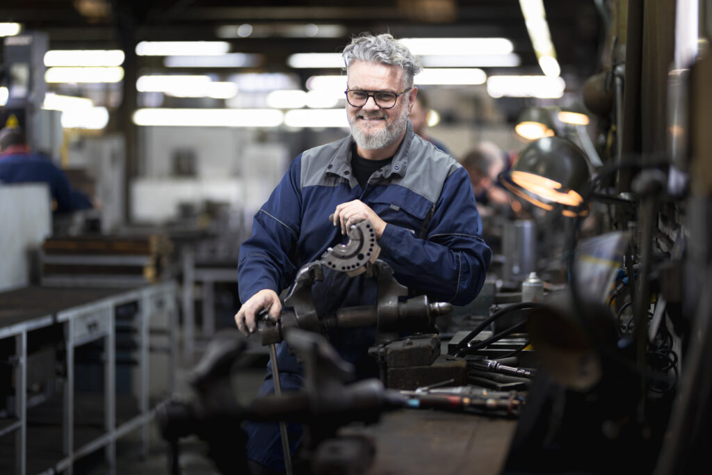 France, Bouttencourt, 2023-02-23. Portrait of a smiling machinist in blue overalls at his lathe in a precision engineeri