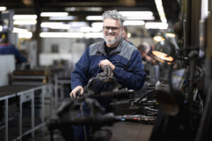 France, Bouttencourt, 2023-02-23. Portrait of a smiling machinist in blue overalls at his lathe in a precision engineeri