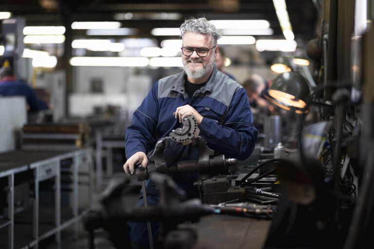 France, Bouttencourt, 2023-02-23. Portrait of a smiling machinist in blue overalls at his lathe in a precision engineeri