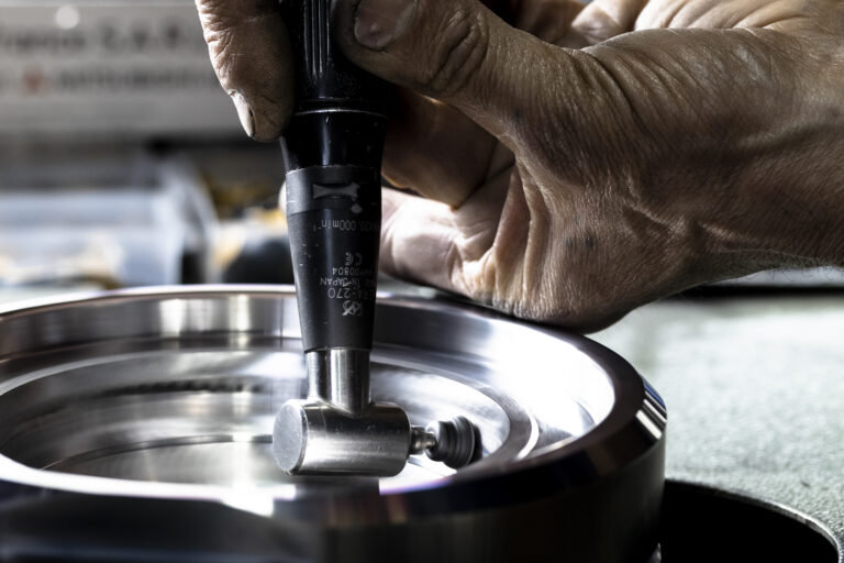 France, Bouttencourt, 2023-02-23. An operator's hands guide a polished stainless steel part into a machine tool, close-u