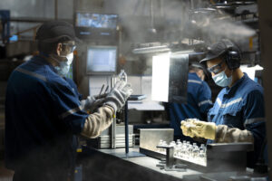 France, Saint-Quentin-la-Motte-Croix-au-Bailly, 2022-04-26. Two workers in blue work clothes and masks work on a product