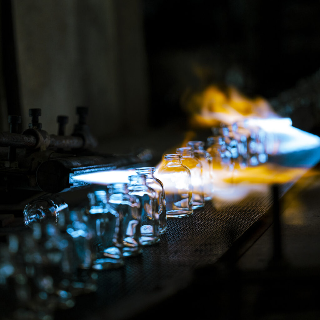 France, Vieux Rouen Sur Bresle, 2022-04-26. Blue and orange torch flames work on glass vials during manufacturing, dark