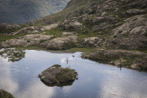 France, Vicdessos, 2023-08-15. A paddle boarder alone on a mountain lake below the Pic des Trois Seigneurs in the Ariege