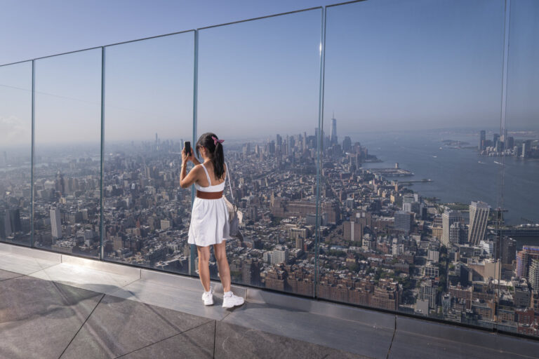 United States, New York, 2026-08-07. A visitor at the sloping glass wall, above the West Side of Manhattan. Photograph b