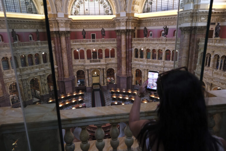 United States, Washington, 2026-08-12. A visitor photographs the Main Reading Room through the glass of the gallery. Pho