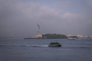 United States, New York, 2026-08-06. A ferry passes in front of the Statue of Liberty under an overcast sky. Photograph