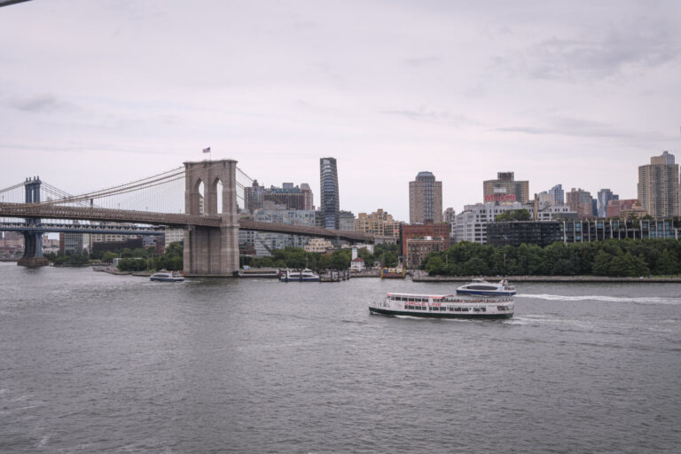 United States, New York, 2026-08-16. A tourist boat sails on the East River in front of the Brooklyn Bridge. Photograph 