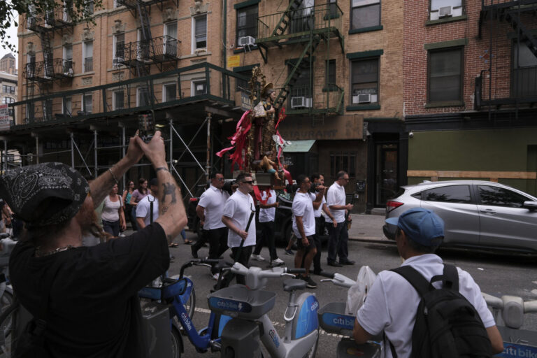 United States, New York, 2026-08-16. A man photographs a religious statue carried during a procession in Little Italy. P