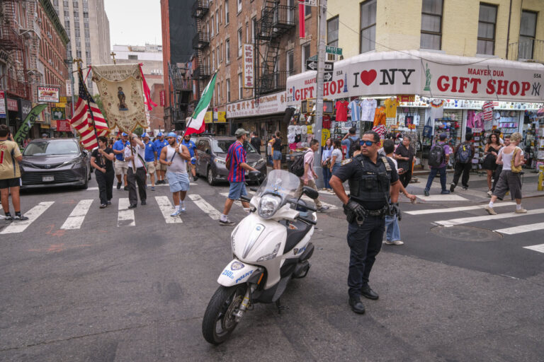 United States, New York, 2026-08-16. The procession crosses an intersection in Chinatown under police escort. Photograph
