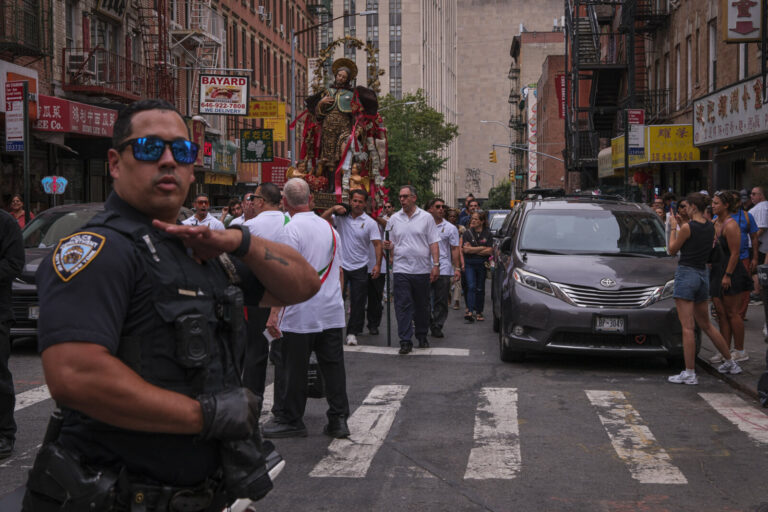 United States, New York, 2026-08-16. A police officer directs traffic as the procession statue advances along a Chinatow
