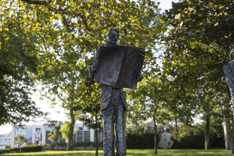 United States, New York, 2026-08-15. The statue of Joseph Pulitzer seen from behind, under the trees of Liberty Island. 