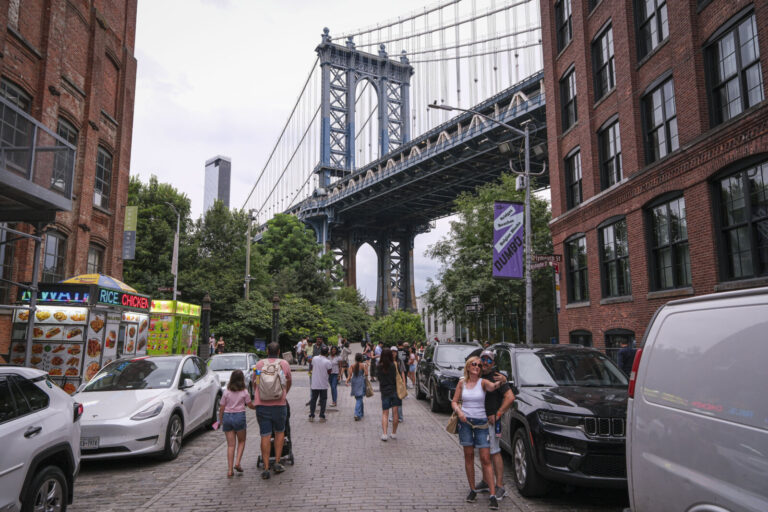 United States, New York, 2026-08-16. A food truck and passers-by on a Dumbo street under the Manhattan Bridge. Photograp