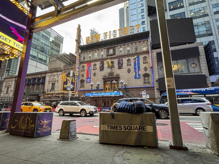 United States, New York, 2026-08-05. A person sleeps on a Times Square barrier in front of the New Victory Theater and t
