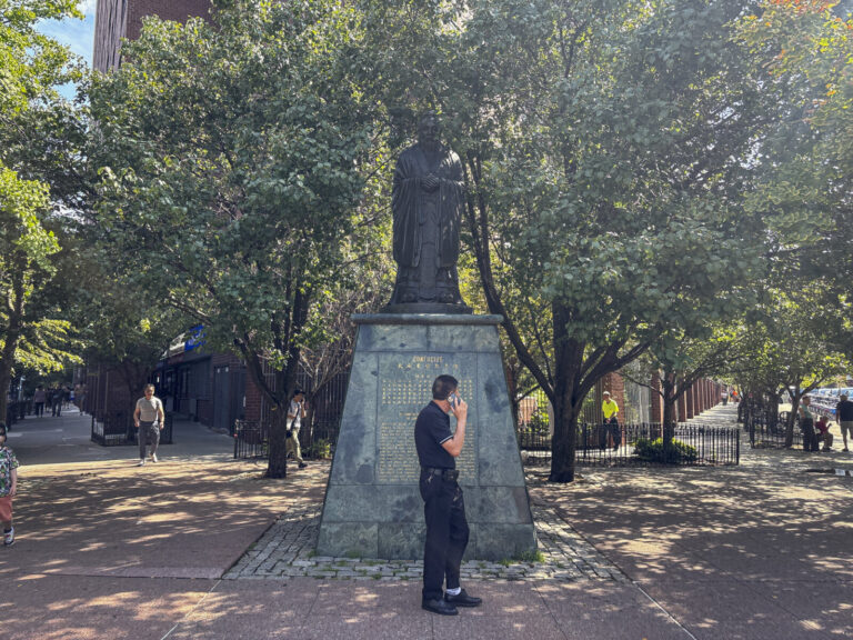 United States, New York, 2026-08-08. A man passes in front of the statue of Confucius on Confucius Plaza in Chinatown. P