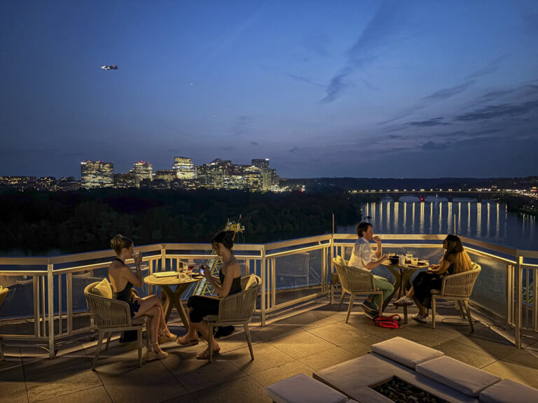 United States, Washington, 2026-08-12. Guests on the rooftop terrace of the hotel at nightfall, facing the Potomac. Phot