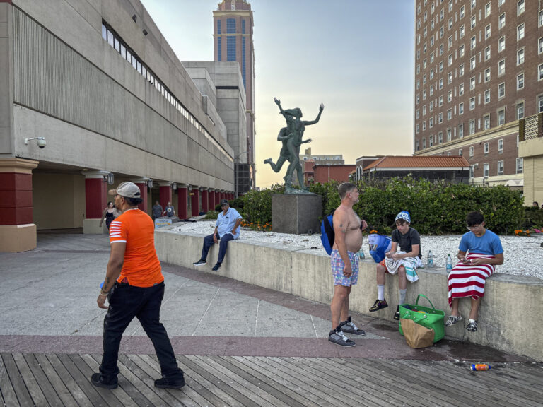 United States, Atlantic City, 2026-08-09. A bronze sculpture stands between the Boardwalk and a car park, where passers-