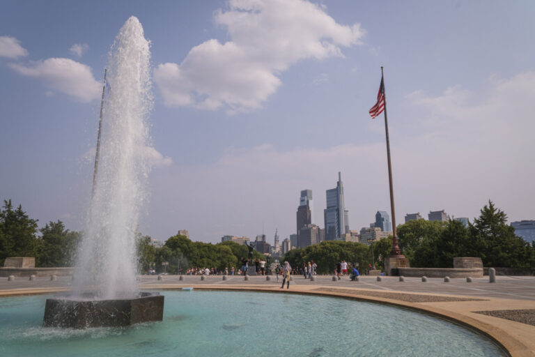 United States, Philadelphia, 2026-08-14. The fountain of Eakins Oval and an American flag, in front of the skyline of Ph