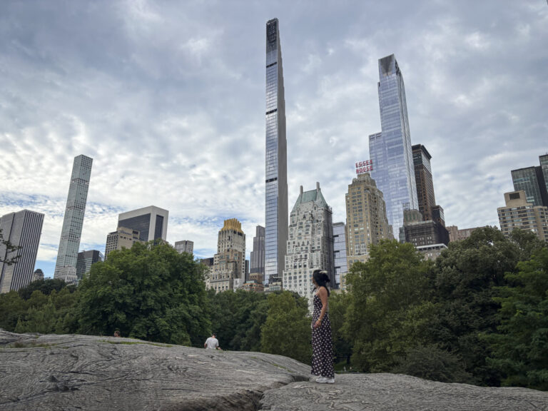 United States, New York, 2026-08-05. A visitor stands on the rocks, silhouetted against the Midtown skyline. Photograph 