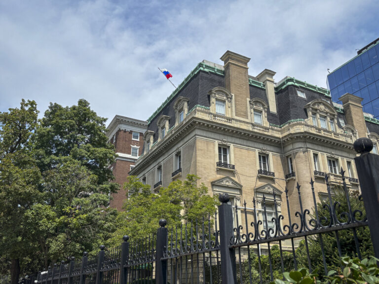 United States, Washington, 2026-08-11. A Beaux-Arts diplomatic building flying a white, blue and red flag, behind its wr