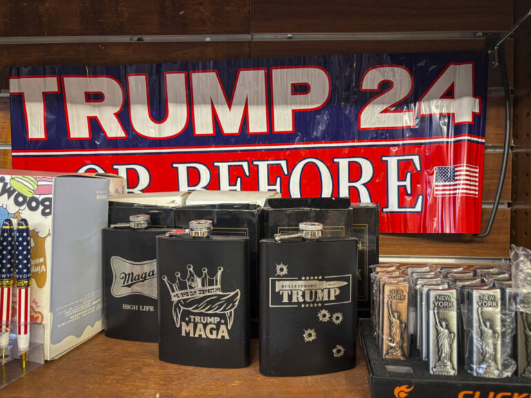 United States, New York, 2026-08-07. A Trump 24 or before banner hangs above hip flasks and souvenirs in a shop in the T