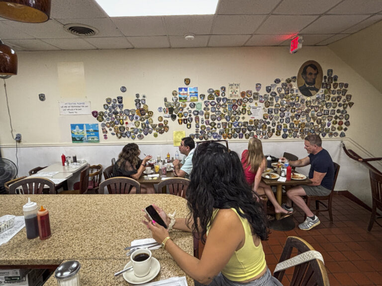 United States, Washington, 2026-08-11. The dining room of a Washington diner, its wall of police patches and its portrai
