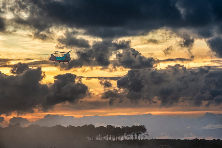 France, Mezos, 2026-09-17. A CH-47D Chinook water-bombing helicopter flies above the forest at sunset during wildfire su