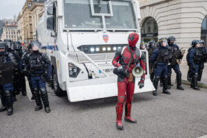 France, Lyon, 2023-03-07. A demonstrator wearing a deadpool costume in front of a riot truck and CRS during the demonstr