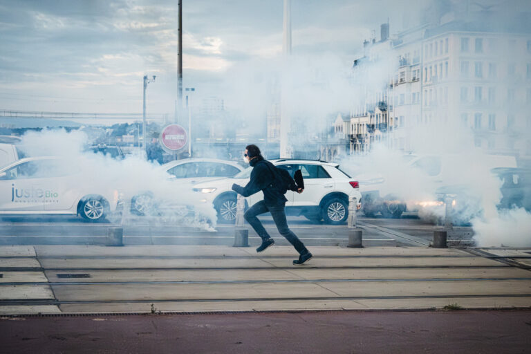 France, Lyon, 2025-09-10. A masked protester runs alone amid tear gas smoke and traffic blockades during the 'Block Ever
