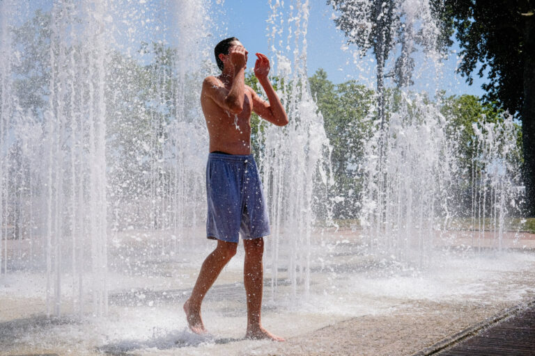 France, Lyon, 2026-06-18. A young man cooling off in the jets of water from a fountain during the heatwave. Photograph b