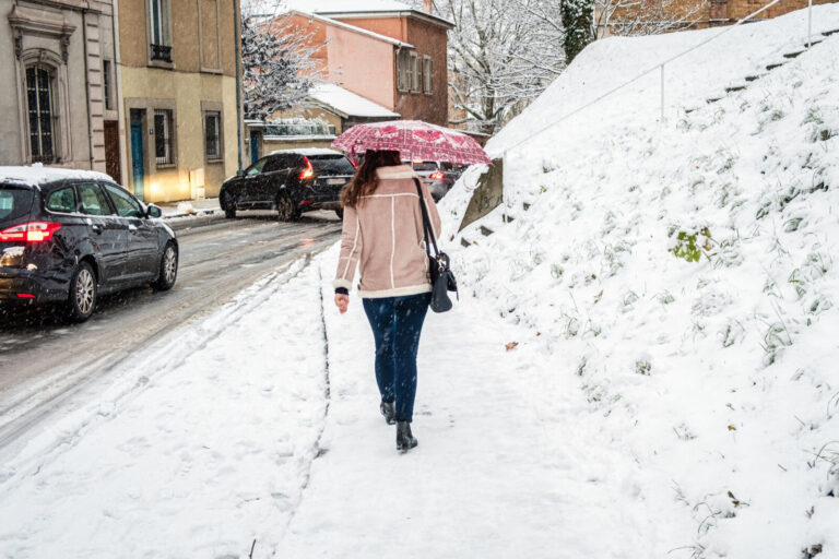France, Lyon, 2017-12-18. A woman from behind with an umbrella walking on snow fallen on a pavement and cars driving on 