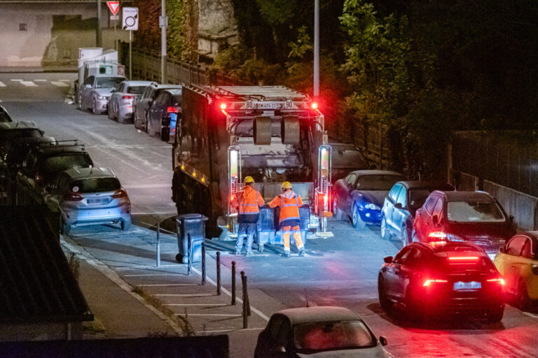 France, Lyon, 2023-11-08. A refuse truck in a street with two refuse collectors bringing the bins to be emptied and a ta