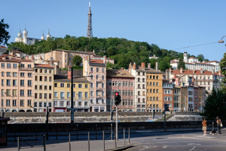 France, Lyon, 2023-06-28. Colourful facades of buildings on the Quai de Saone and two passers-by waiting to cross the st