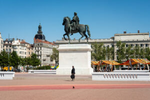 France, Lyon, 2026-04-23. Place Bellecour with its equestrian statue of King Louis XIV and a pedestrian walking past. Ph