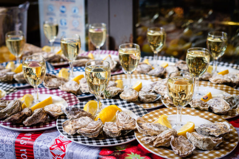France, Lyon, 2024-02-16. Plates of oysters with lemons and glasses of white wine on a table outside a restaurant. Photo
