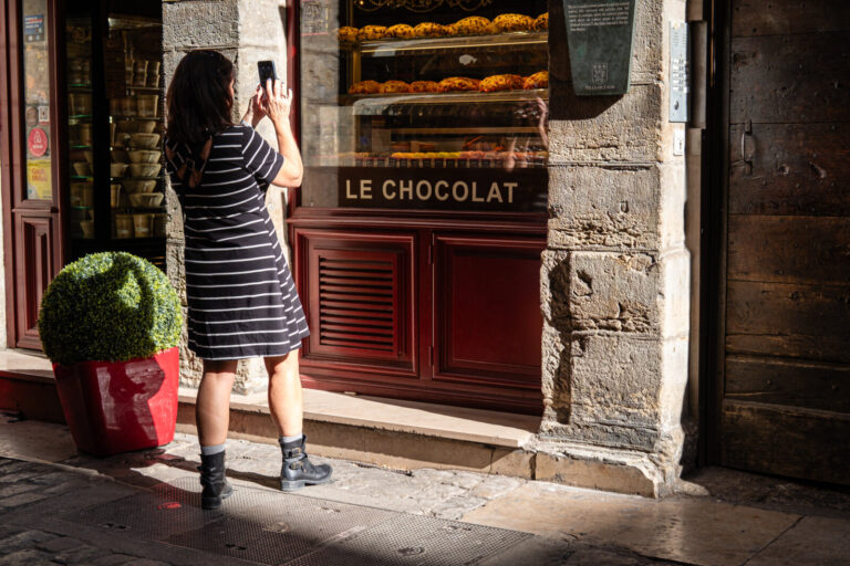 France, Lyon, 2023-10-09. A woman from the back taking a photo with her mobile phone of a shop window with cakes in old 