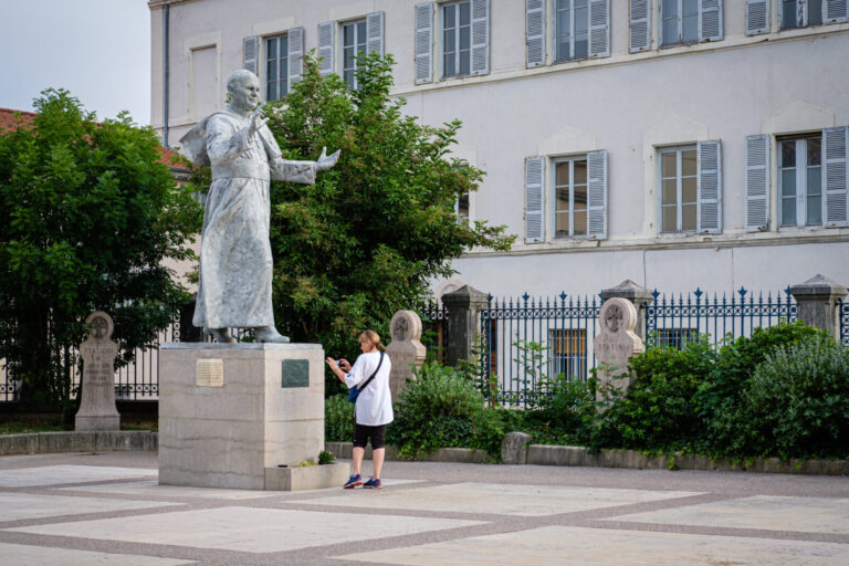 France, Lyon, 2024-06-26. A woman taking a photo with her mobile phone of the statue of Pope John Paul II on the forecou