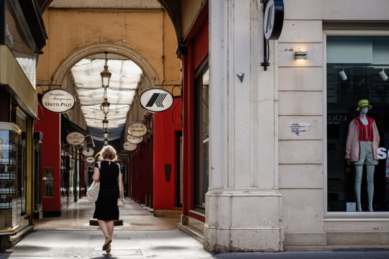 France, Lyon, 2024-06-26. A woman from behind entering the Passage de l'Argue shopping centre with a mannequin in a shop