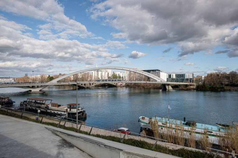 France, Lyon, 2025-02-26. View of the Raymond Barre bridge with a tram crossing and below the Rhone and barges on the qu
