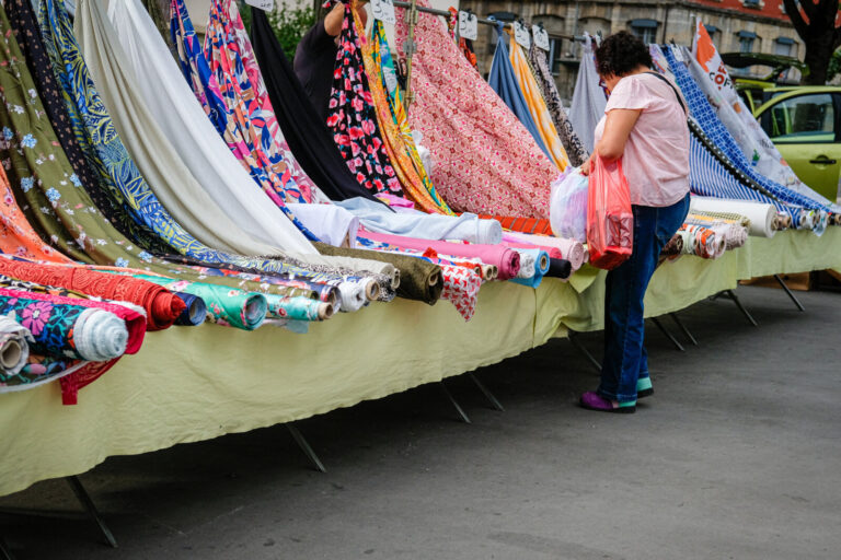 France, Lyon, 2025-07-07. A customer looking at rolls of fabric at a market. Photography Franck CHAPOLARD / Collectif DR