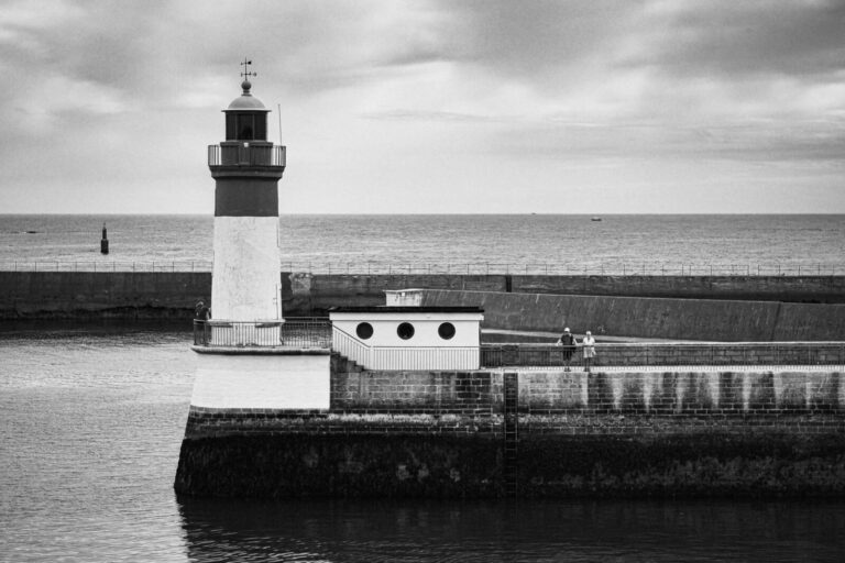 France, Guilvinec, 2026-08-04. A couple standing on the harbour quay next to the lighthouse. Photograph by Franck CHAPOL