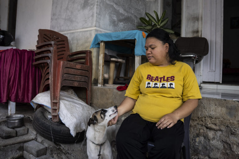 Indonesia, Tomohon, 2026-09-12. Portrait of Gratia, a Minahasa againt dog meat, petting her dog outside her house, a con
