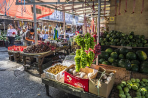 Indonesia, Tomohon, 2026-08-29. Fruit stall with a pyramid of watermelons, hanging bunches of grapes, customers choosing