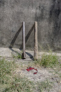 Indonesia, Langowan, 2026-09-12. Two slaughter posts, one metal and one wooden, leaning against a wall with blood traces