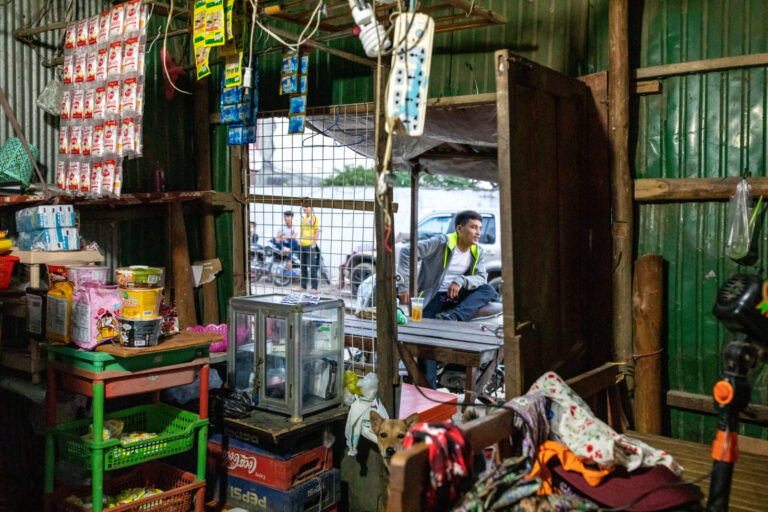 Cambodia, Phom Penh, Tuol Kok, 2019-11-29. View from inside a grocery store, a passer-by is visible through the window. 