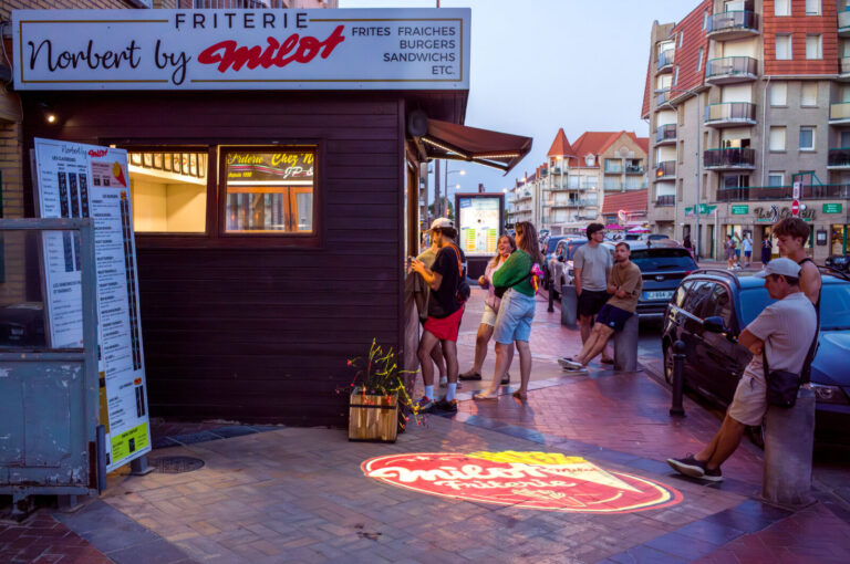 France, Bray-Dunes, 2026-08-09. Holidaymakers queue outside the Norbert by Milot chip shop in the evening. Traditional f
