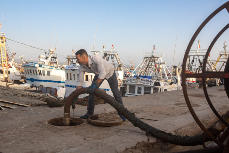Morocco, Essaouira, 2019-09-26. A sailor fills up with fuel with a long hose, facing an armada of trawlers moored becaus