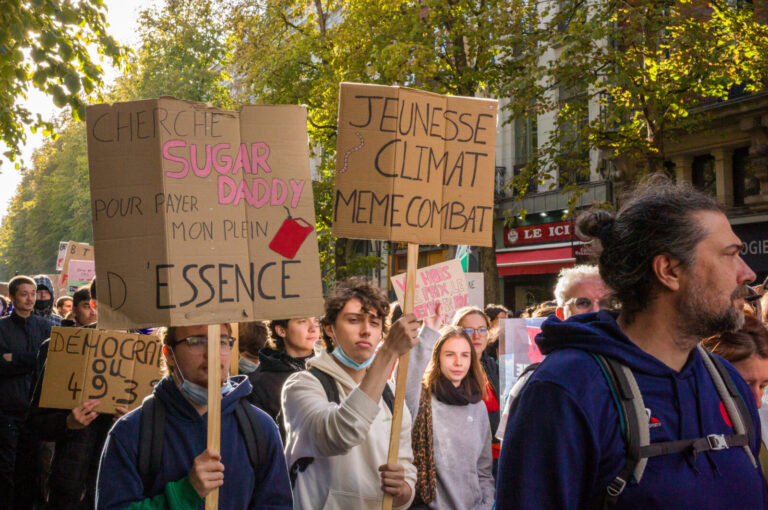 France, Lille, 2026-10-17. Marchers carry signs about petrol costs and a shared youth and climate struggle along a tree-