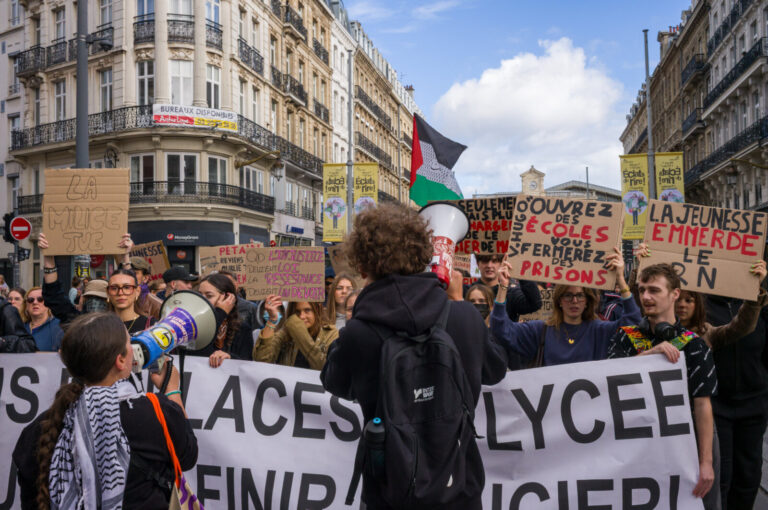 France, Lille, 2026-10-17. Two protesters hold megaphones facing a group carrying a white banner and signs about schools